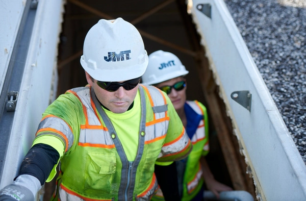Two people in hard hats and safety vests walking up stairs