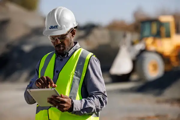 Employee in PPE looking at tablet on site