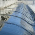 Water flowing over the curved concrete spillway of a dam.